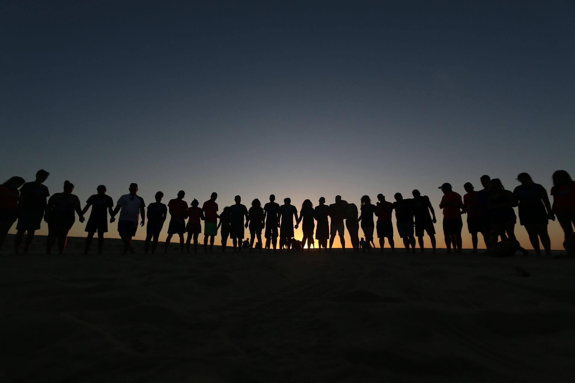 A sun set and on the horizon there are silhouettes of people holding hands.