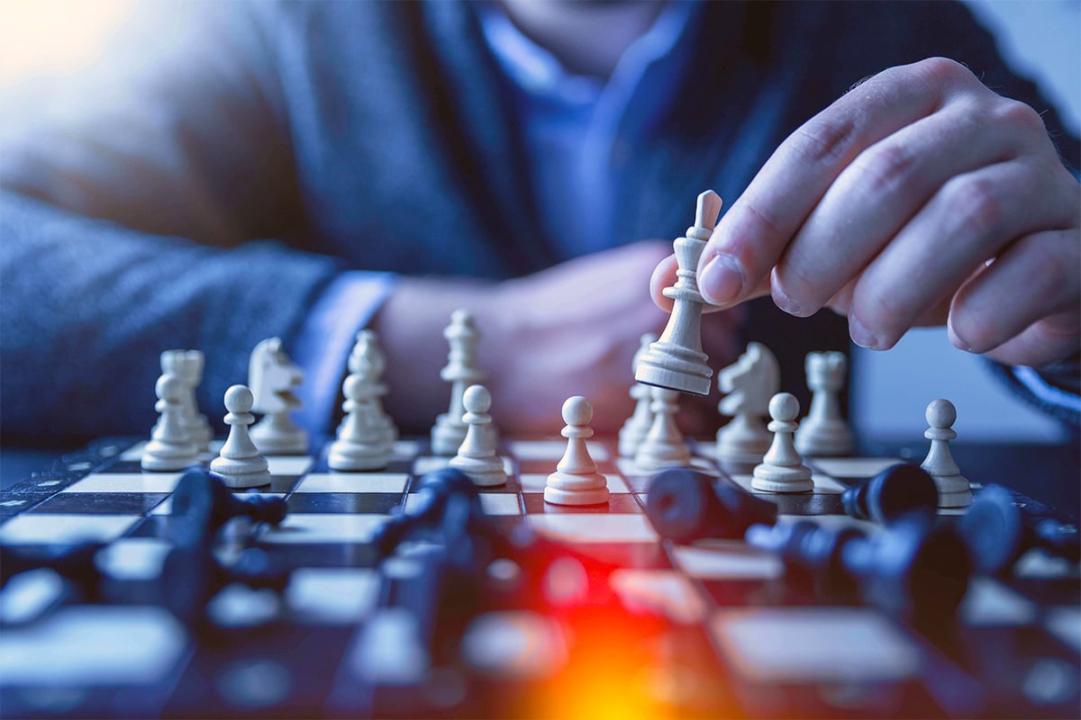 A person playing chess and making move with a white figure. He seems to be dominating because most of the black figures have fallen.